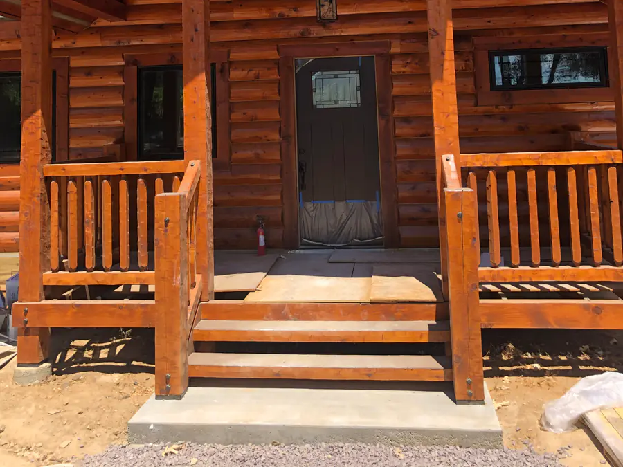 The entry porch of a D-log home: rounded log courses either side of the door and log-post railings on the steps.