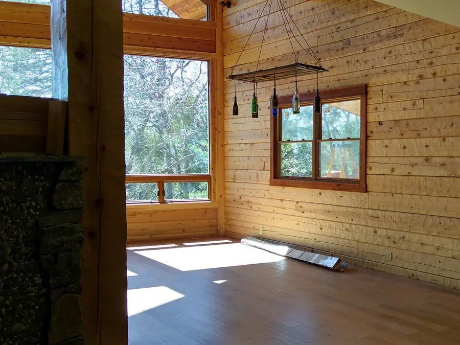 An empty room inside a D-log home, the flat interior log wall and a window into the trees.