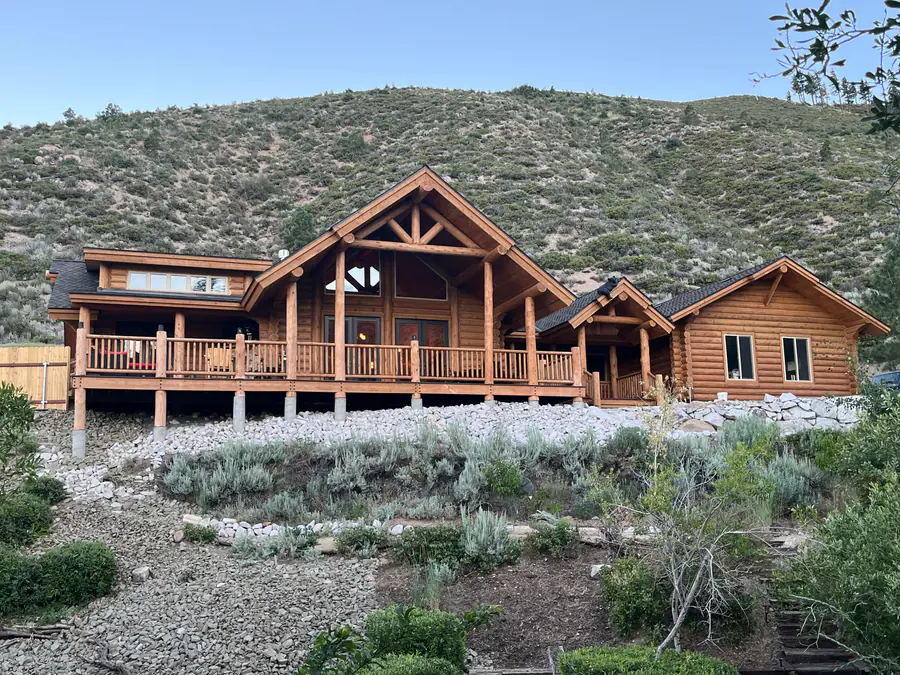 A long round log lodge with a covered porch across its front, set into a dry canyon slope.