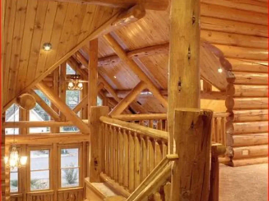 A stair hall inside a finished log home, log balusters on the stair and warm light on the log walls.